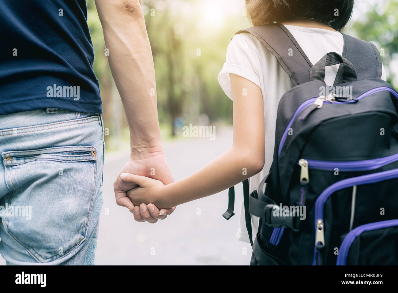 Asian father's hand lead his girl child in summer park go to school. Trust family and back to school concept. Stock Photo