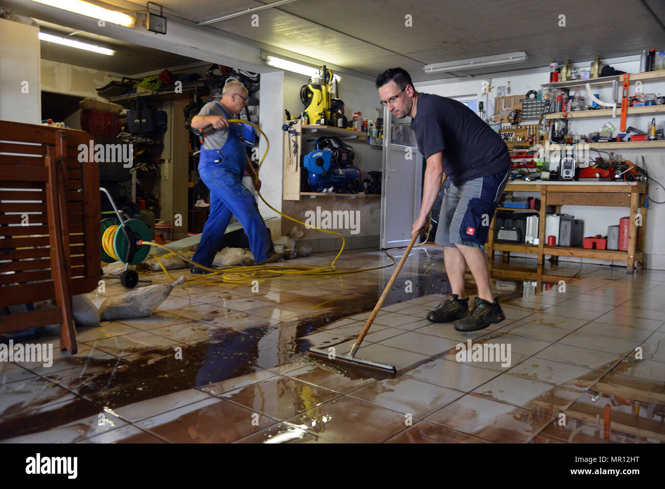 25 May 2018, Germany, Trassem: Benny Hein (r) and Alfred Fuelling clearing up in the garage. Heavy rain caused a landslide in Trassem in western Germany, which damaged several properties. Photo: Harald Tittel/dpa Stock Photo