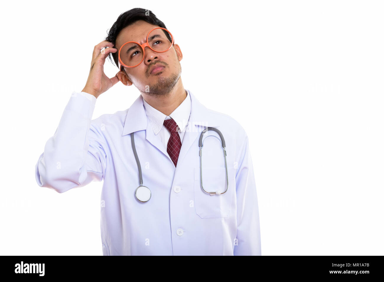 Studio shot of young Asian man doctor thinking while scratching  Stock Photo