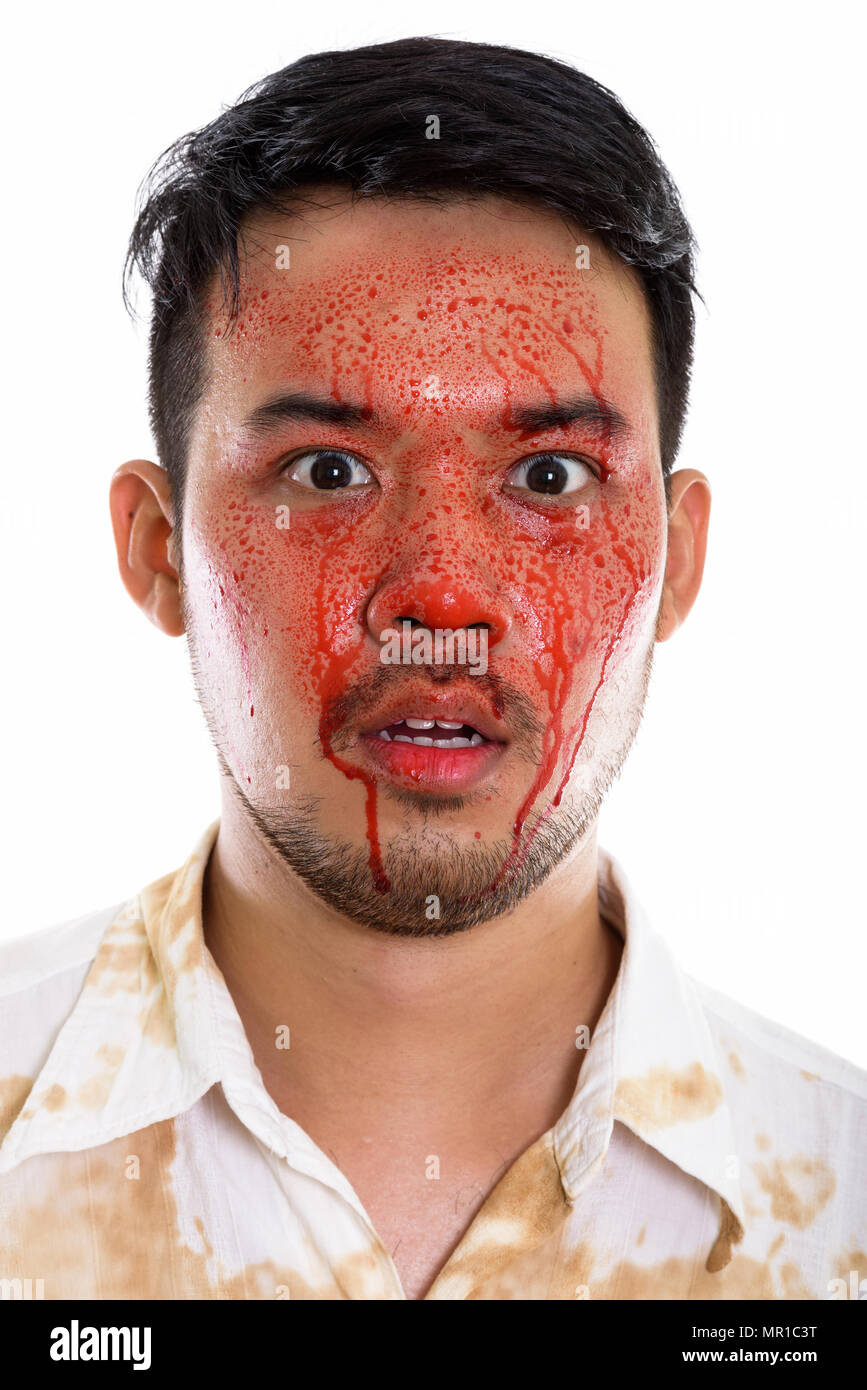 Face of young crazy Asian man looking shocked with blood on face Stock Photo