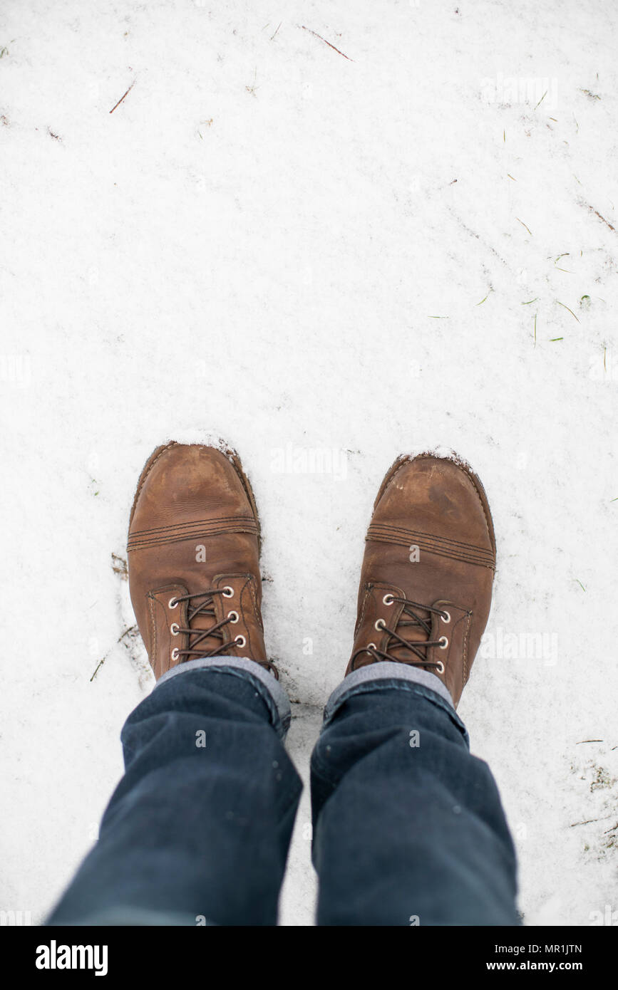 Feet of a man wearing Red Wing work boots and blue jeans standing in snow. Stock Photo