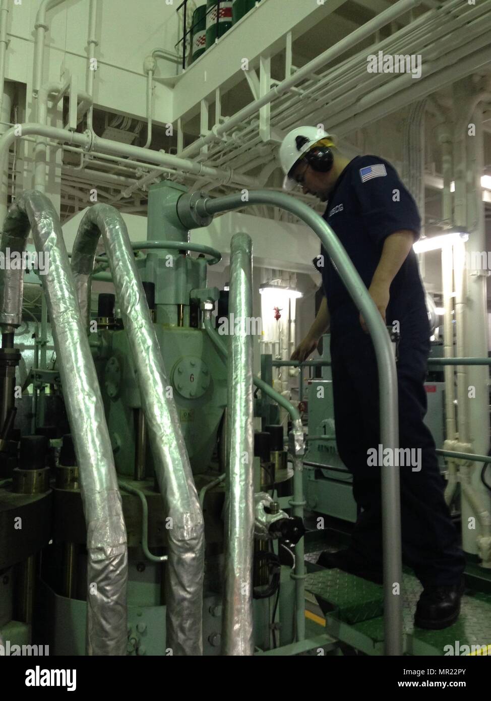 Petty Officer 1st Class Andrew Christopherson, a marine science technician at Coast Guard Marine Safety Unit Portland, inspects a component in the engine room of the vessel Port Belmonte during a Port State Control exam at the Port of Portland, Ore., May 1, 2017.    The engine room of a vessel has many potential fire hazards that need to be inspected for fuel leaks or combustion hazards. Stock Photo