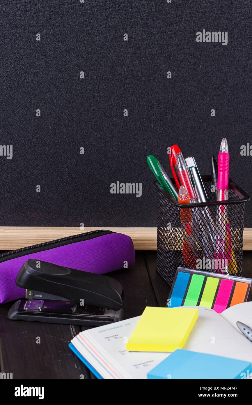 Pencil case with various stationery on old wooden table, on blackboard background Stock Photo