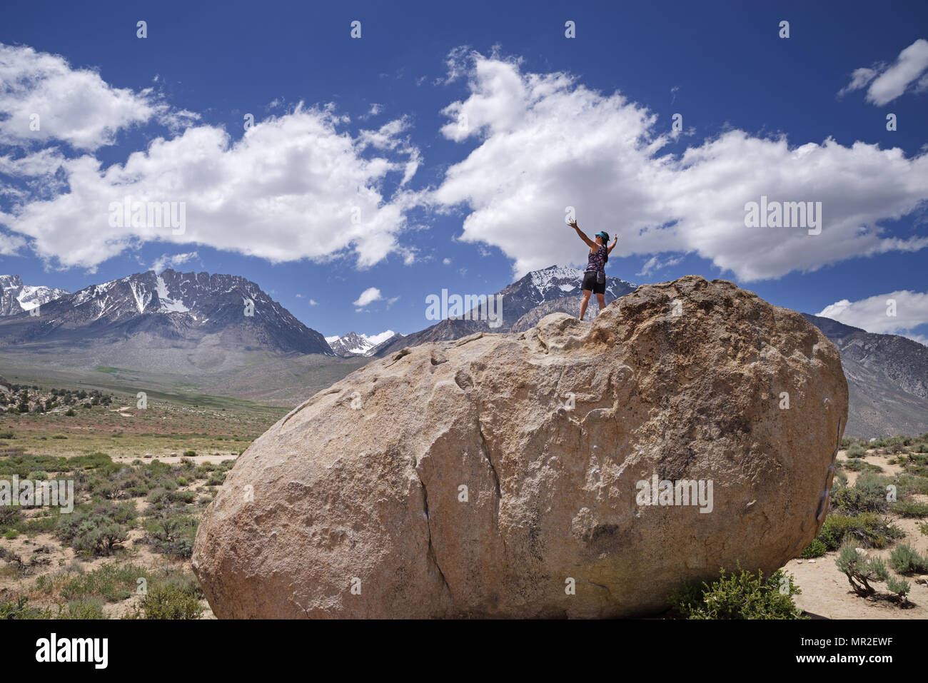 a woman on top of a boulder embraces nature with both arms Stock Photo