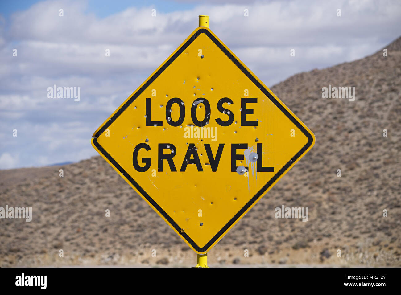 loose gravel road sign with bullet holes and out of focus desert hill and sky behind it Stock Photo