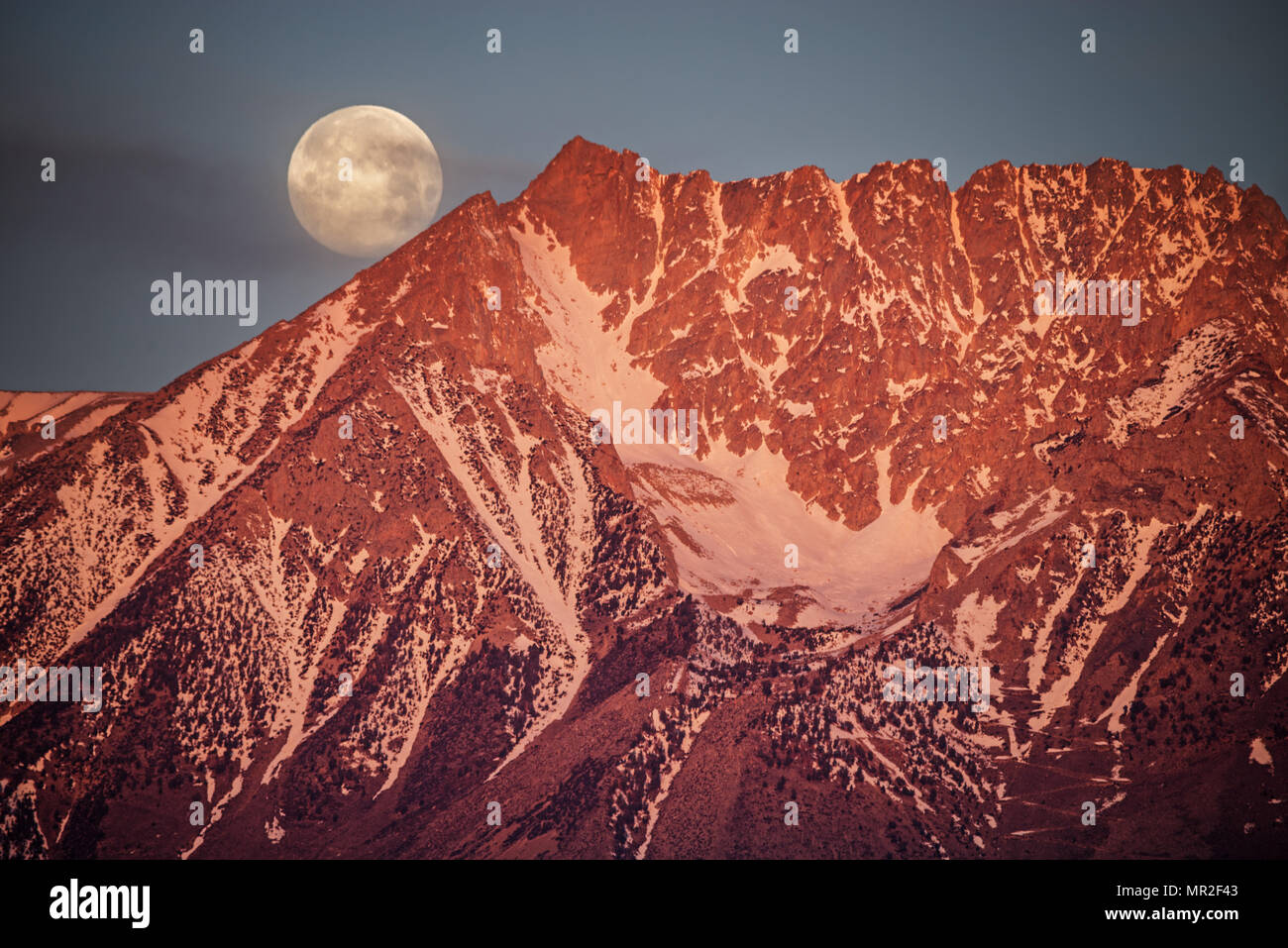 full moonset behind Basin Mountain at sunrise in the Sierra Nevada Mountains west of Bishop California Stock Photo