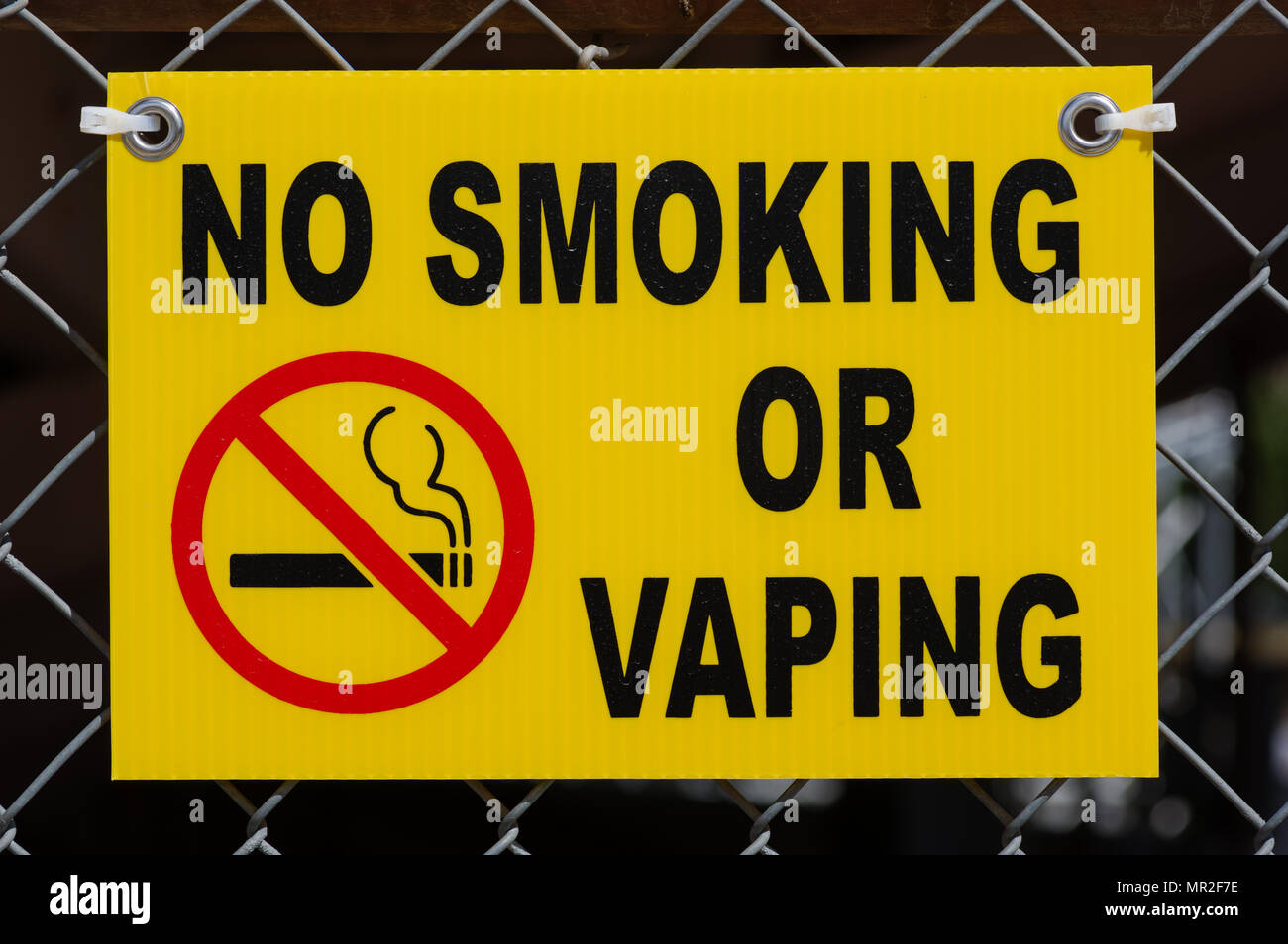 yellow no smoking or vaping sign fastened to a chain-link fence Stock Photo