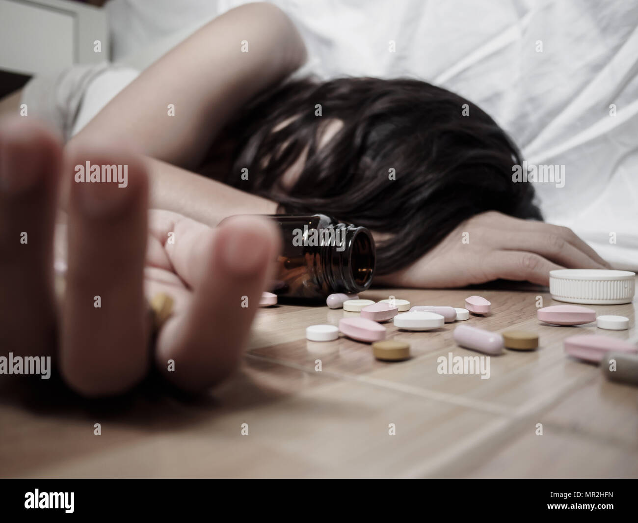 Young woman is lying on the floor with a lot of pills. Overdose and suicide concept. Stock Photo