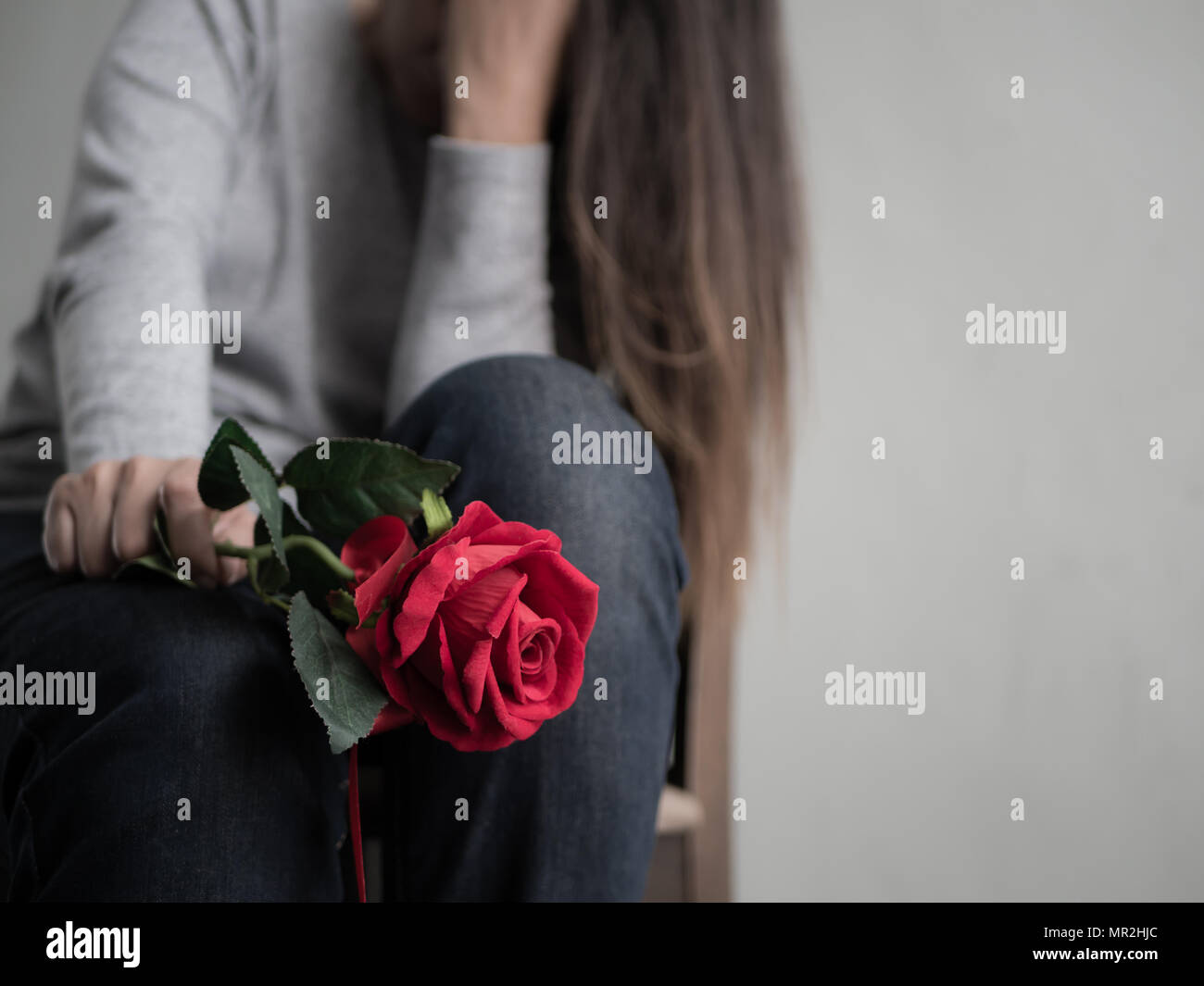 Sad woman sitting and crying with red rose in her hand. Lonly ...