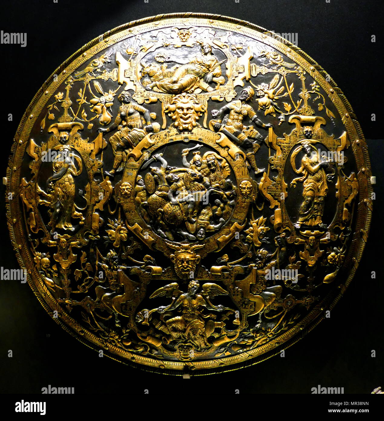parade shield, dated 1554 by Giorgio Ghisi (1520 — 1582), Italian engraver from Mantua who also worked in Antwerp and in France. The shield, now part of the Waddesdon Bequest, is made of iron, hammered in relief, damascened with gold and partly plated with silver. It has an intricate design with a scene of battling horseman in the centre, within a frame, around which are four further frames containing allegorical female figures, the frames themselves incorporating minute subjects from the Iliad and ancient mythology, inlaid in gold. Stock Photo