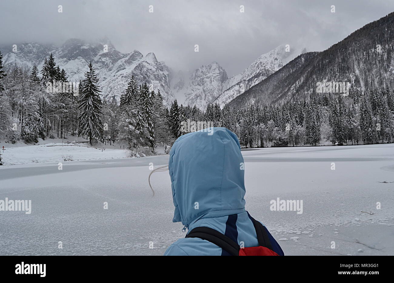 Person With Hood In Front Of A Frozen Lake In The Mountains Covered In Snow Fusine Italy Stock Photo Alamy