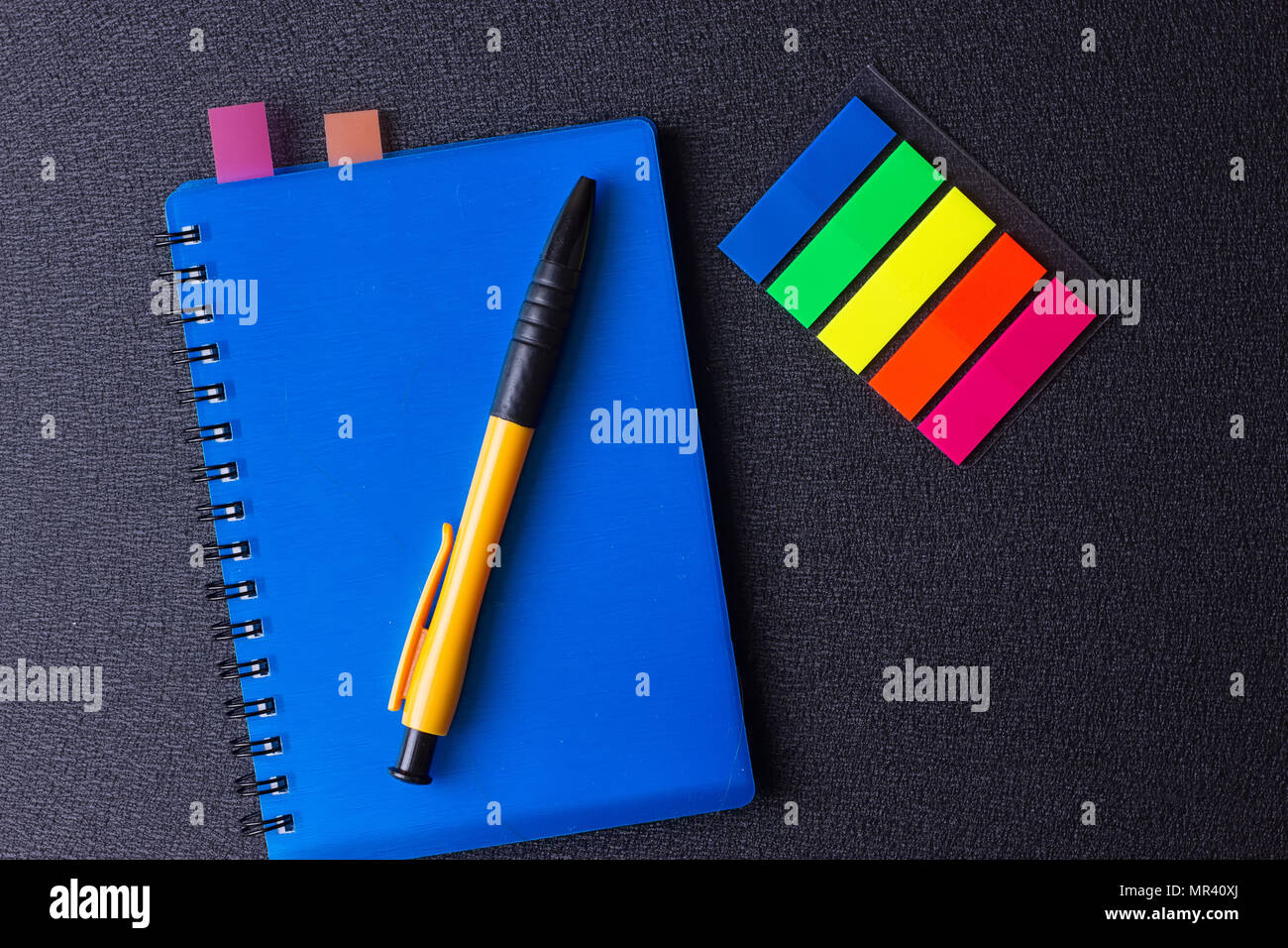 Blue notepad with multi-colored stickers and pen on a black background Stock Photo