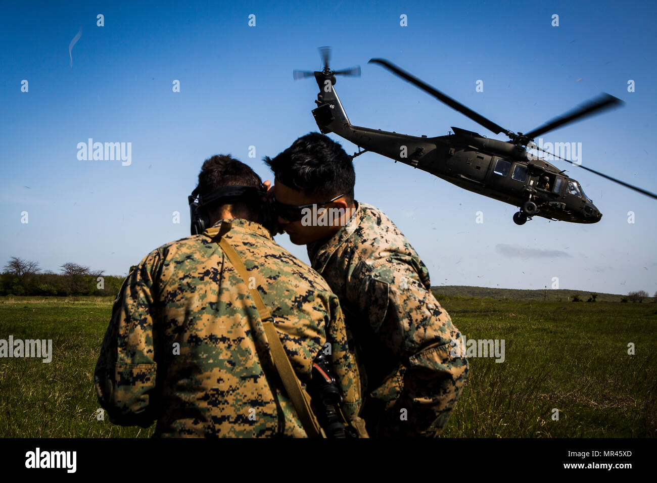 U.S. Marine Sgt. Viktor Cadiente, a forward observer with Black Sea Rotational Force 17.1, teaches Lance Cpl. Tyler Holloway, a rifleman with Marine Rotational Force Europe 17.1, how to call in a landing of a U.S. Army UH-60 Blackhawk helicopter over the radio during Exercise Platinum Eagle 17.2 at Babadag Training Area, Romania, April 30, 2017. Marines with MRF-E and BSRF participate in Exercise Platinum Eagle 17.2, a multilateral exercise held with NATO Allies and partner nations to improve interoperability and effectiveness. Strong NATO relationships are vital to not only European security, Stock Photo