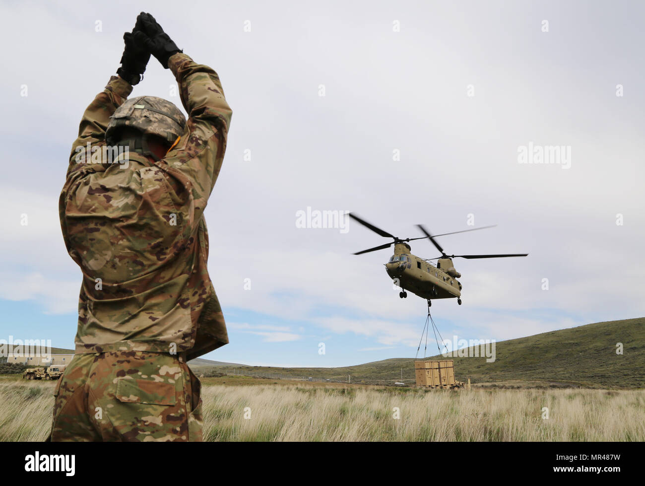 U.S. Army Pvt. Travis Botson, 92nd Chemical Company, 33rd Chemical Battalion, 48th Chemical Brigade, gives arm and hand signals to a CH-47 Chinook during a sling load operation at the Yakima Training Center, Yakima, Wash., May 5, 2017. Sling load operations allow units to accomplish their mission by rapidly relocating supplies and equipment, bypassing surface obstacles. (U.S. Army photo by Sgt. Kalie Jones) Stock Photo