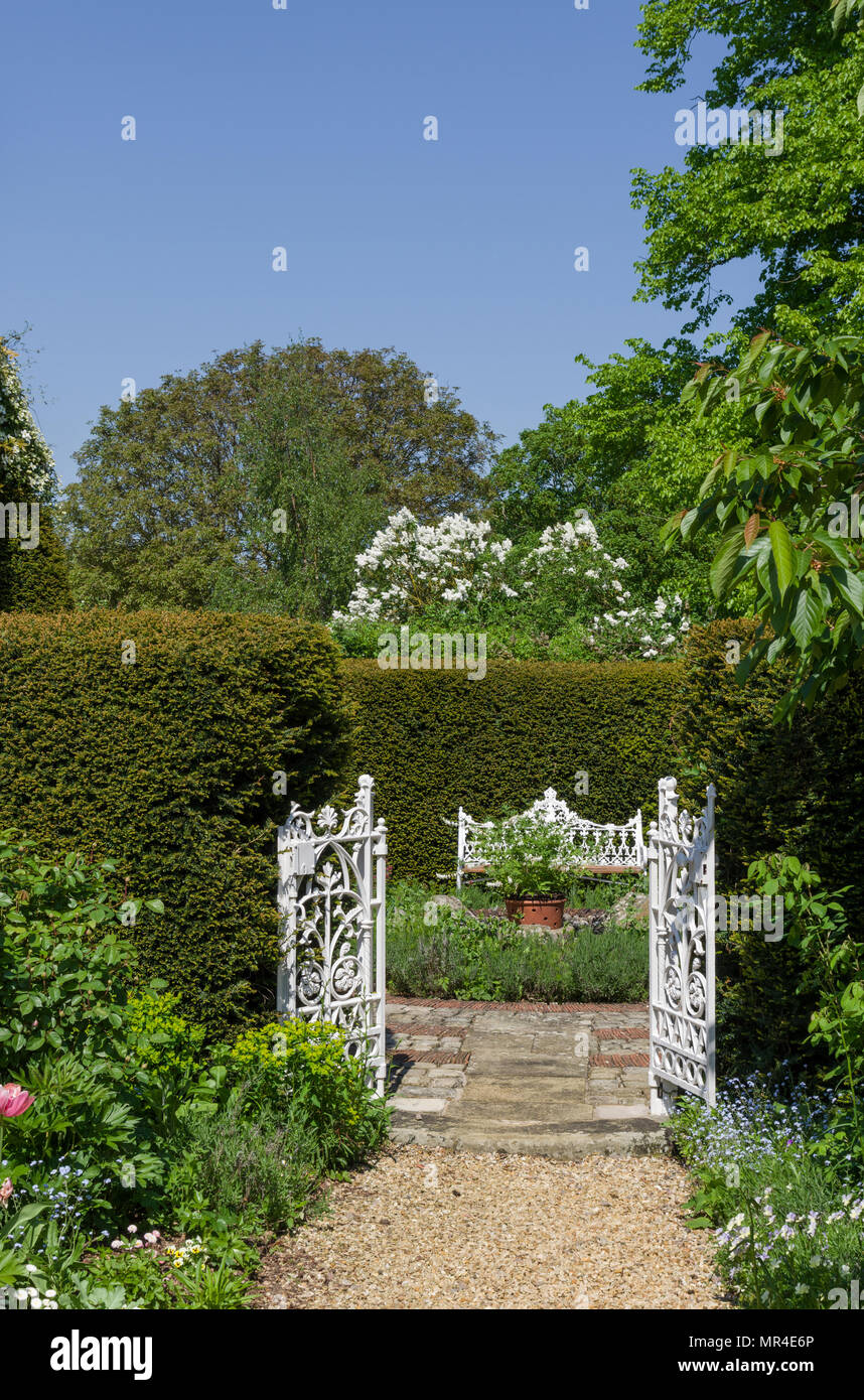 Open white gates leading into the formal garden with a white seat opposite; part of Kathy Brown's Garden, Stevington, Bedfordshire, UK Stock Photo