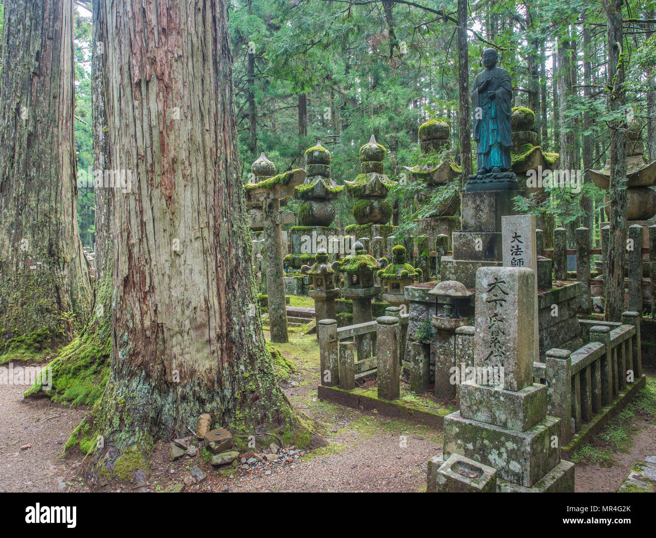 Bronze statue of Kobo Daishi, with giant sugi trees and moss covered gorinto five-tiered stupas, and memorial gravestones,  Okunoin, Koya-san,Wakayama Stock Photo
