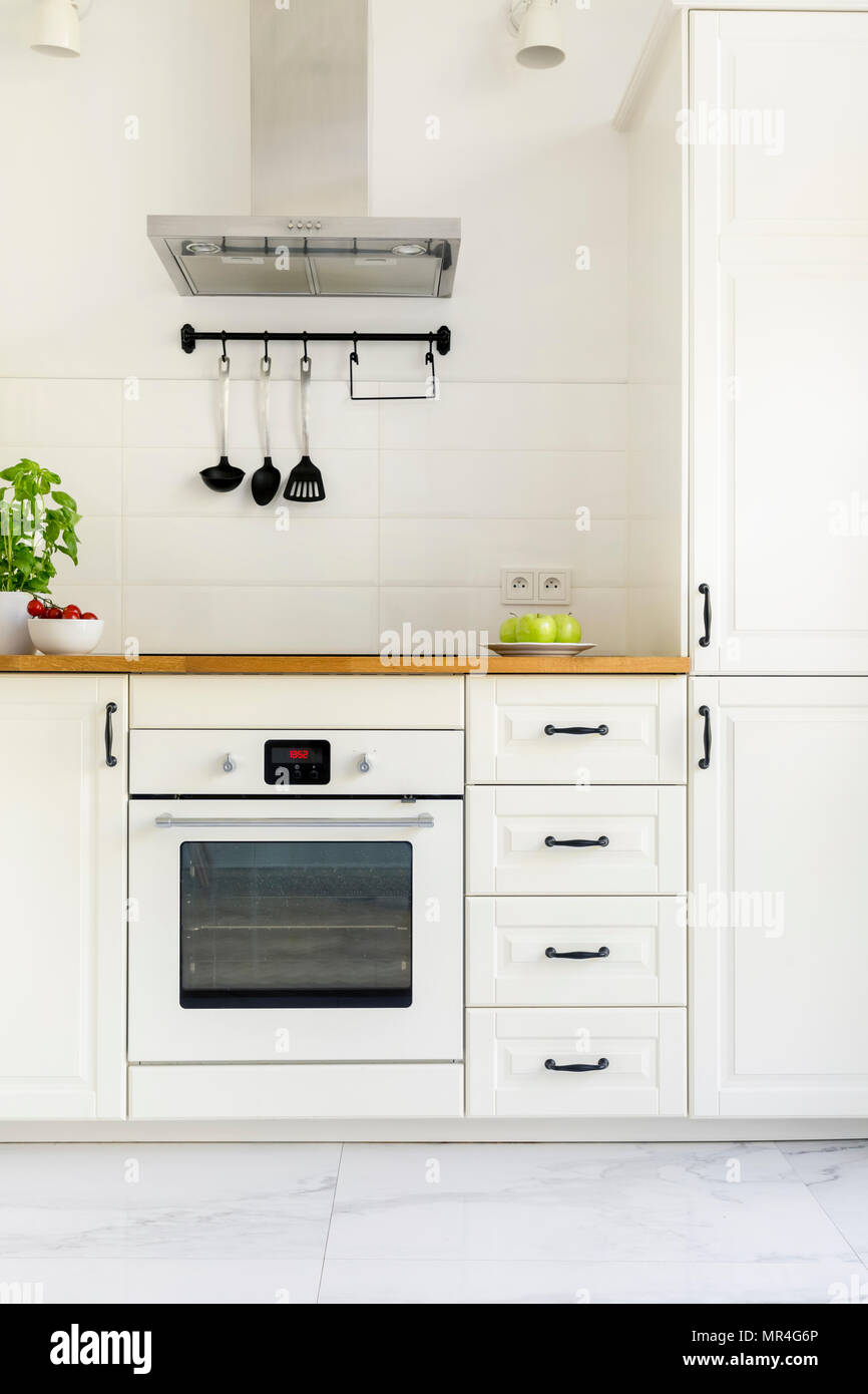 White cabinet in minimal kitchen interior with wooden countertop. Real photo Stock Photo