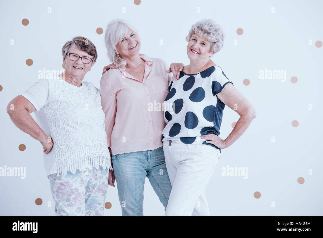Group of friendly senior women enjoying meeting against white wall with gold dots Stock Photo