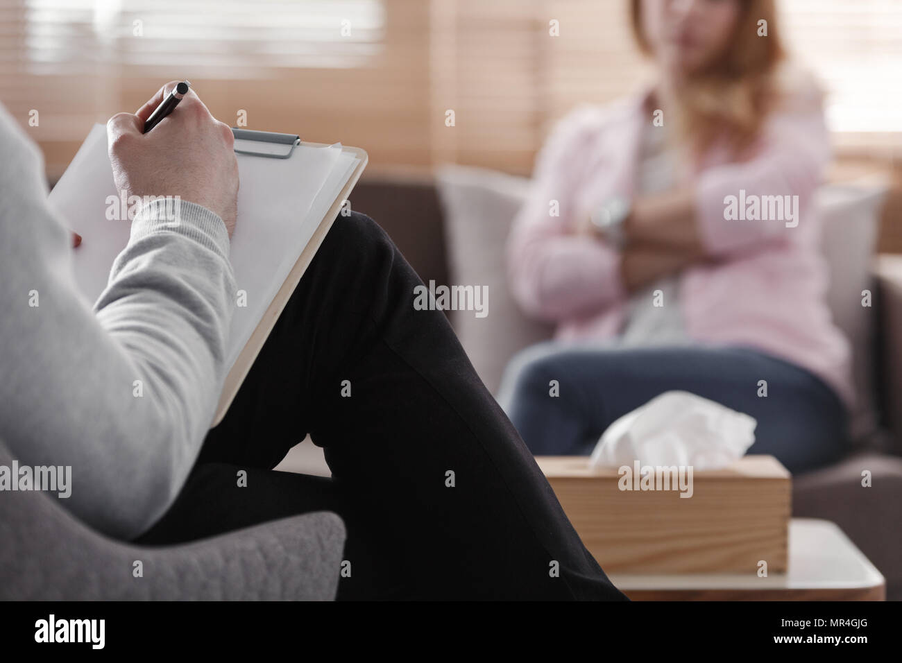 Back view of psychotherapist writing notes, assessing patient's health and giving diagnosis to a woman sitting on a couch in the blurred background du Stock Photo