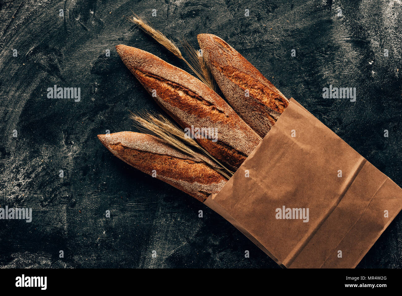 top view of arranged french baguettes in paper bag and wheat on dark tabletop with flour Stock Photo