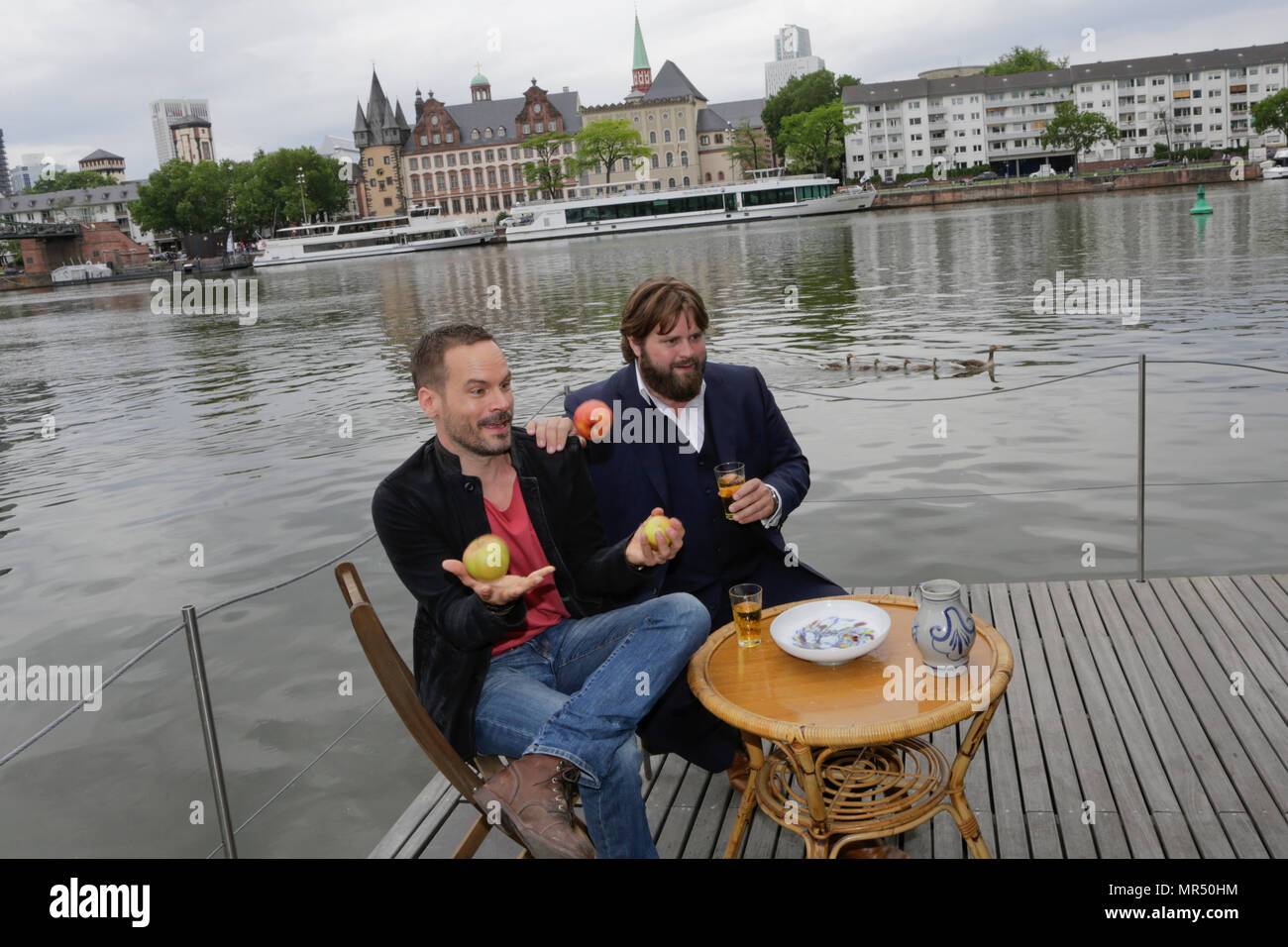 Actors Wanja Mues (left) and Antoine Monot, Jr. (right) pose on the terrace of the houseboat that is owned by Mues' character Leo in the TV show with two glasses of cider and a Bembel (a local type of stoneware jug, used for cider).  Wanja Mues juggles three apples. 4 new episodes of the relaunch of the long running TV series 'Ein Fall fuer zwei’ (A case for two) are being filmed in Frankfurt for the German state TV broadcaster ZDF (Zweites Deutsches Fernsehen). It stars Antoine Monot, Jr. as defence attorney Benjamin ‘Benni’ Hornberg and Wanja Mues as private investigator Leo Oswald. The epis Stock Photo