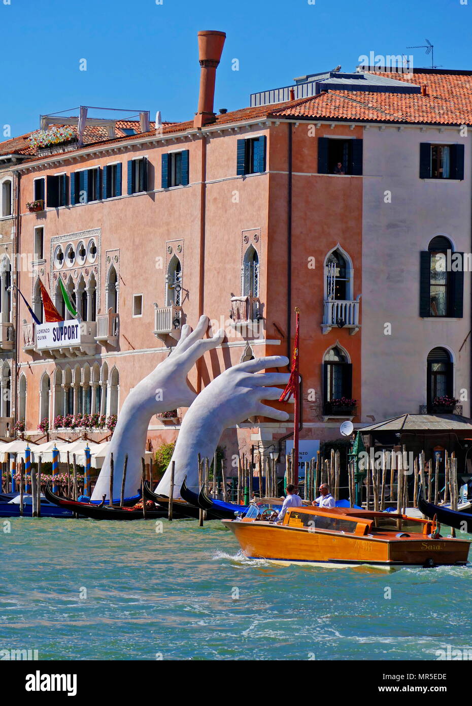 A sculpture of large hands emerges from the grand canal, seemingly supporting and bracing the ca’ sagredo hotel, Venice. By Lorenzo Quinn (born May 7, 1966), Italian sculptor and son of actor Anthony Quinn Stock Photo