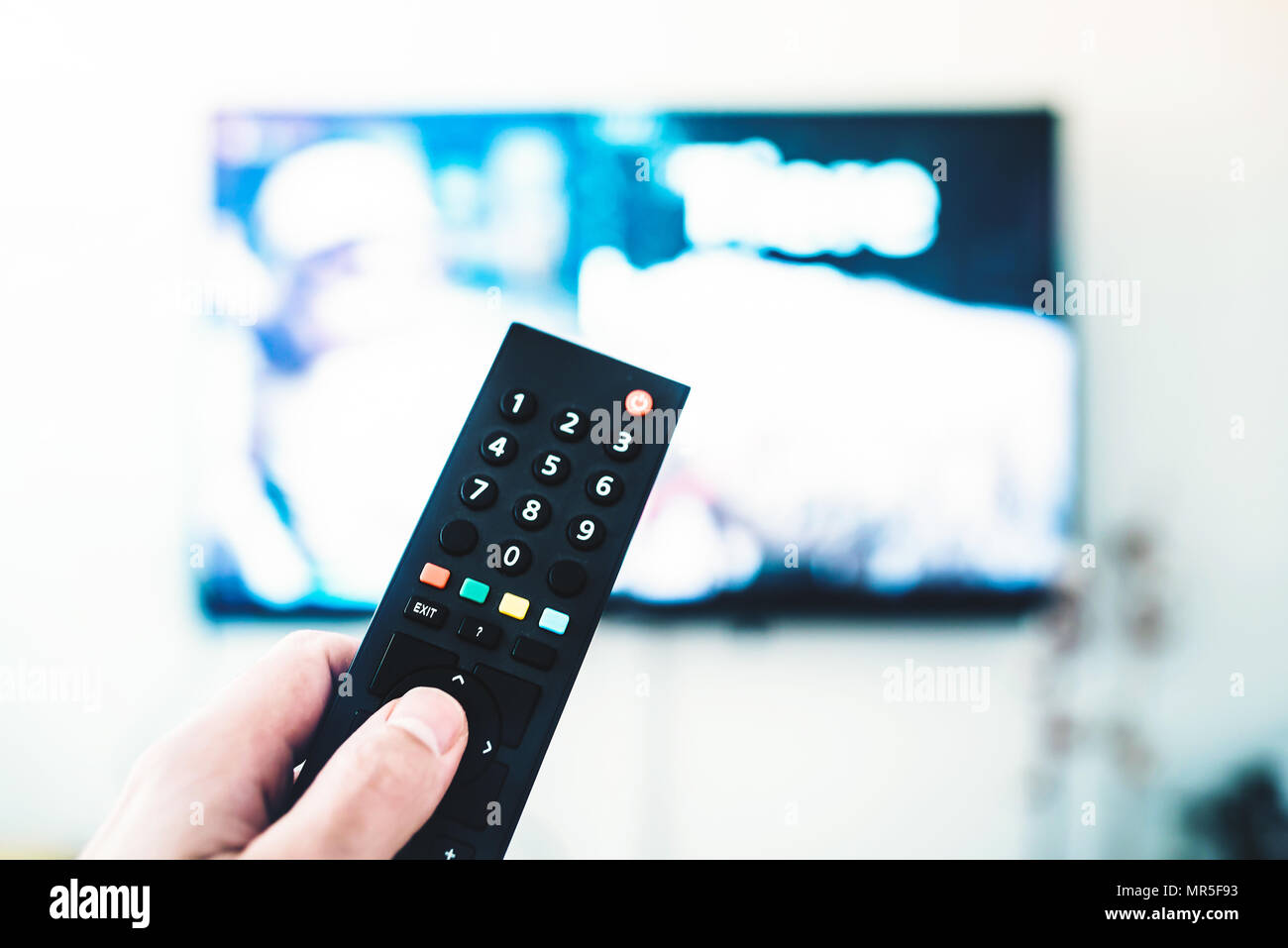 person using remote control against TV on white wall Stock Photo