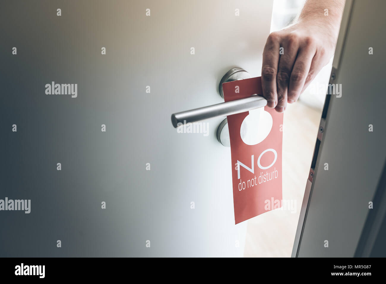 hand placing red do not disturb sign on handle of hotel room door Stock Photo