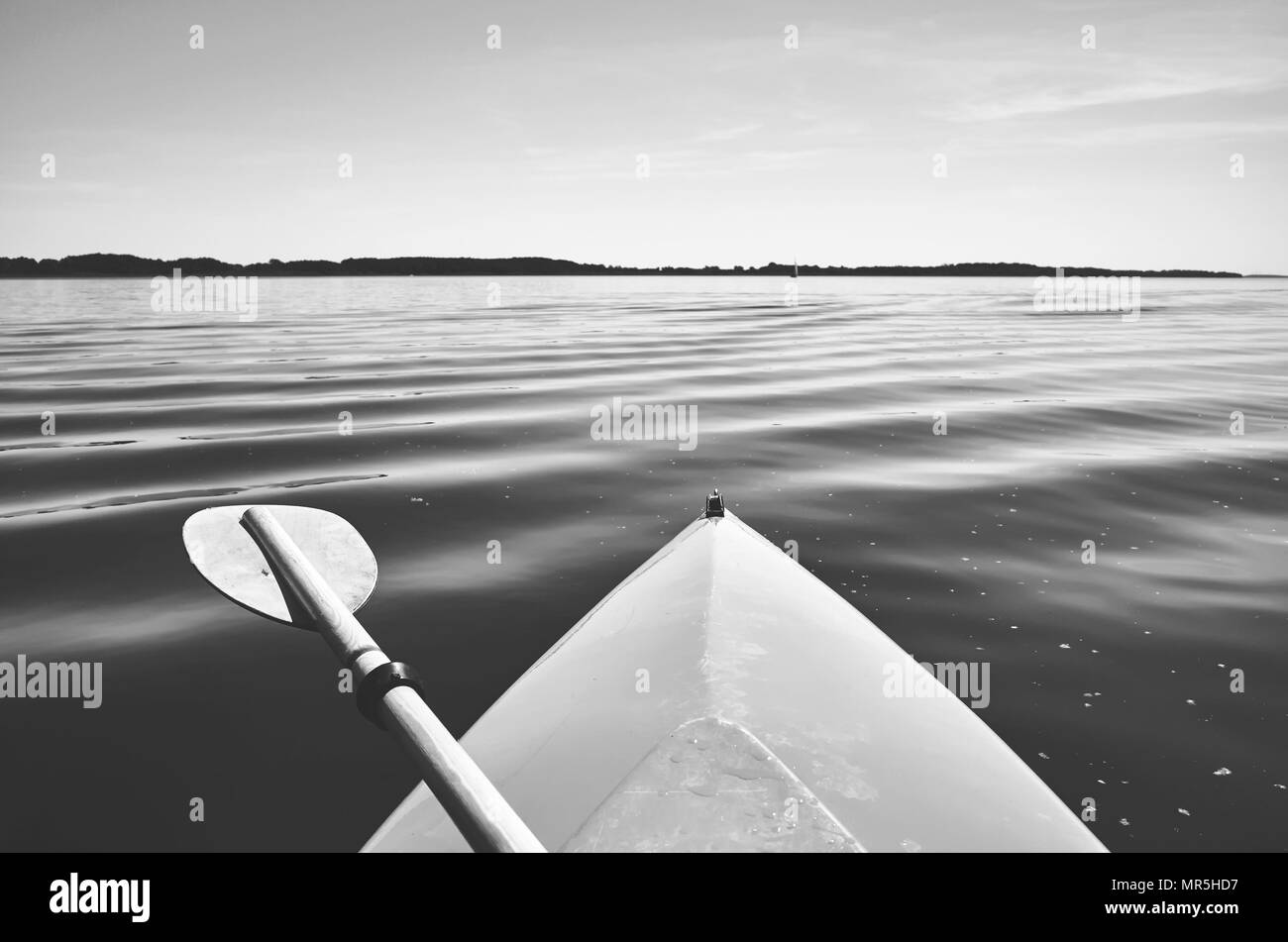 Retro stylized picture of a bow of a kayak with paddle on a lake, selective focus. Stock Photo