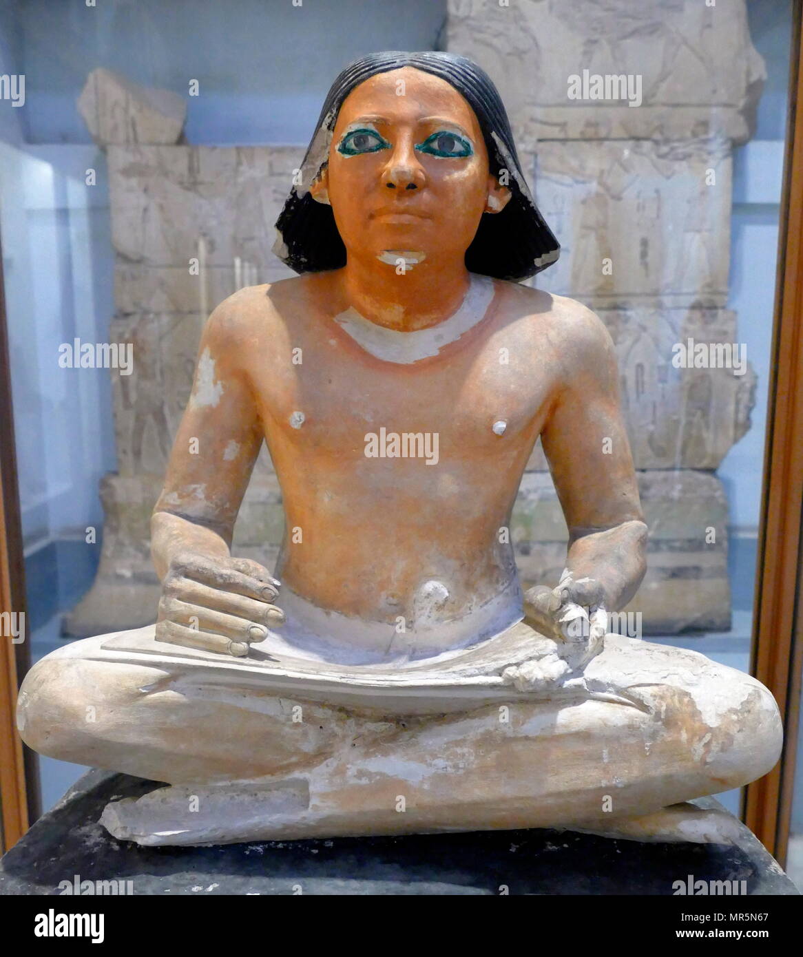painted limestone statue of an Egyptian scribe seated cross-legged holding an open papyrus scroll. 5th Dynasty, Saqqara. Stock Photo