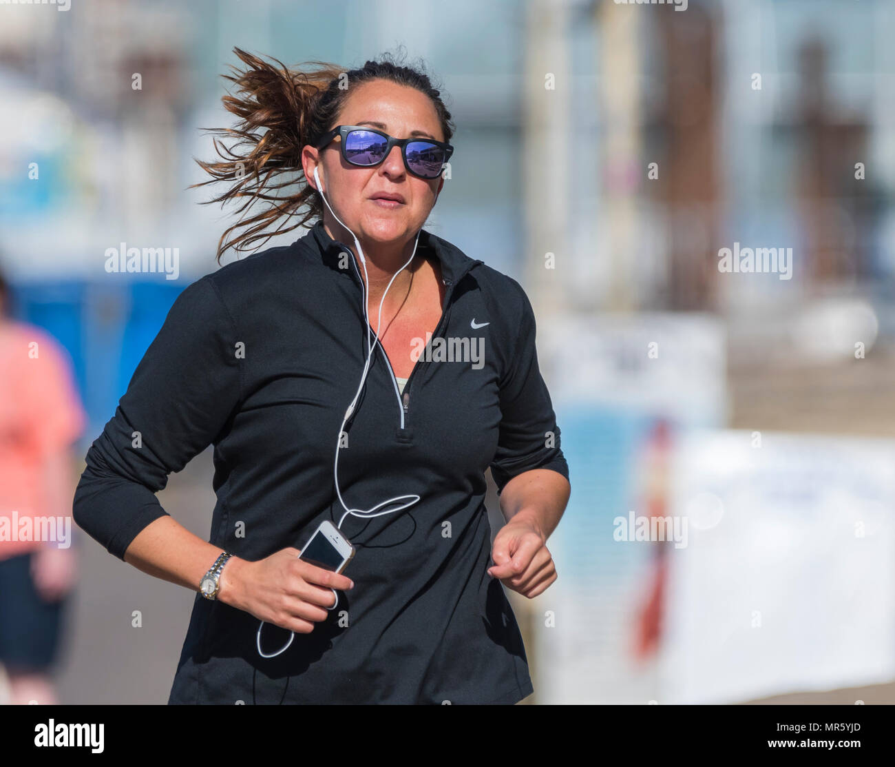 Woman wearing black and sunglasses taking a morning job listening to music on headphones in the UK. Healthy lifestyle. Stock Photo