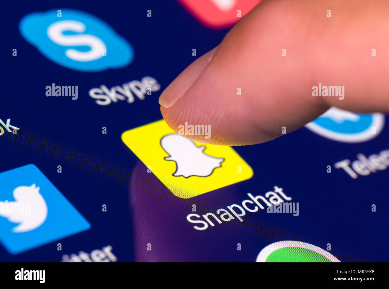Finger pressing Snapchat app icon on a mobile device or tablet. Using snapchat. Stock Photo
