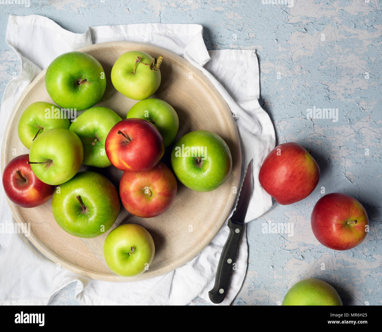 Green cooking apples and red eating apples with a knife against a blue