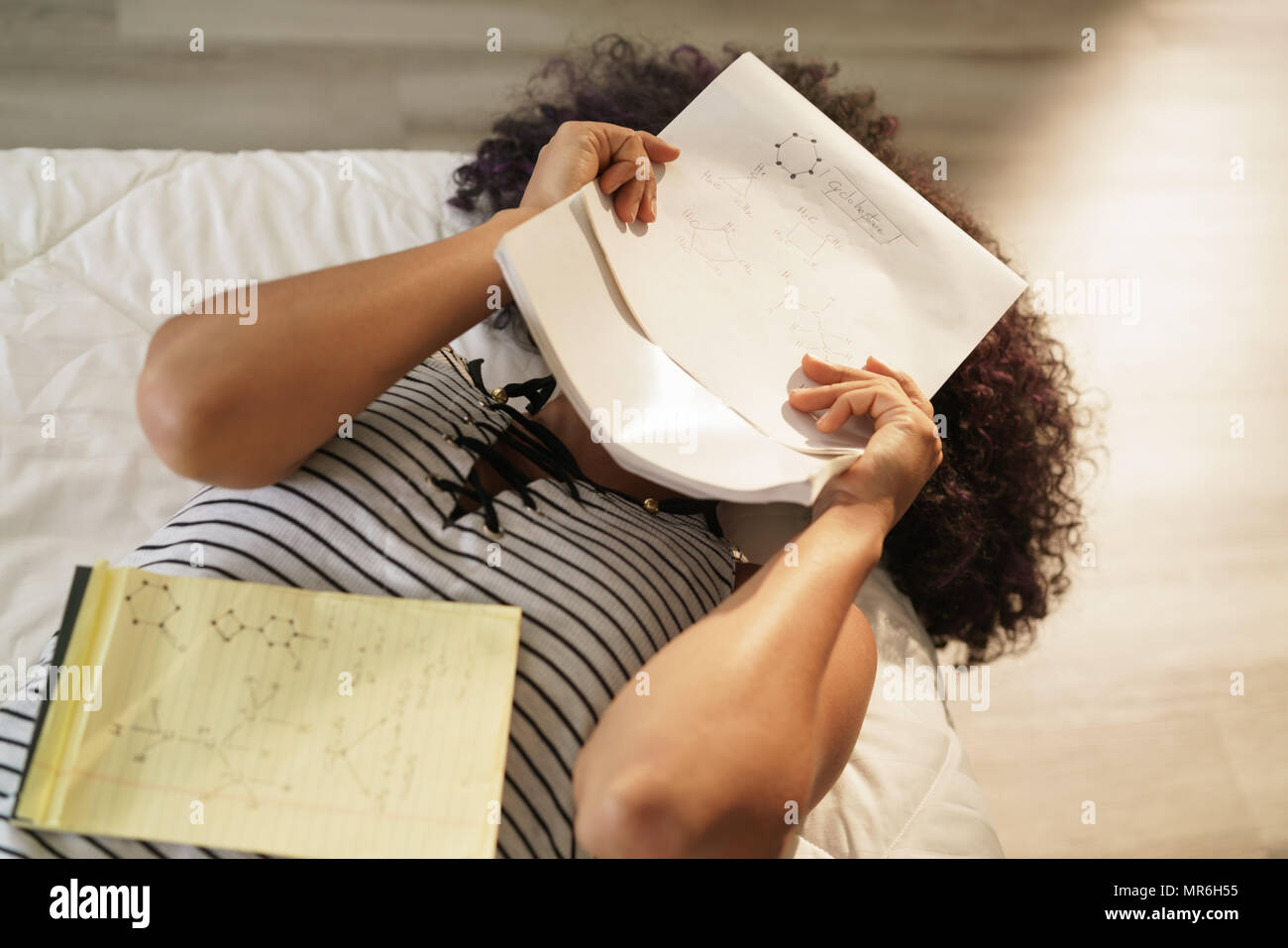 African american college student doing homework in bed at home. Black woman studying chemistry formulas, having problems to memorize notes on exercise Stock Photo