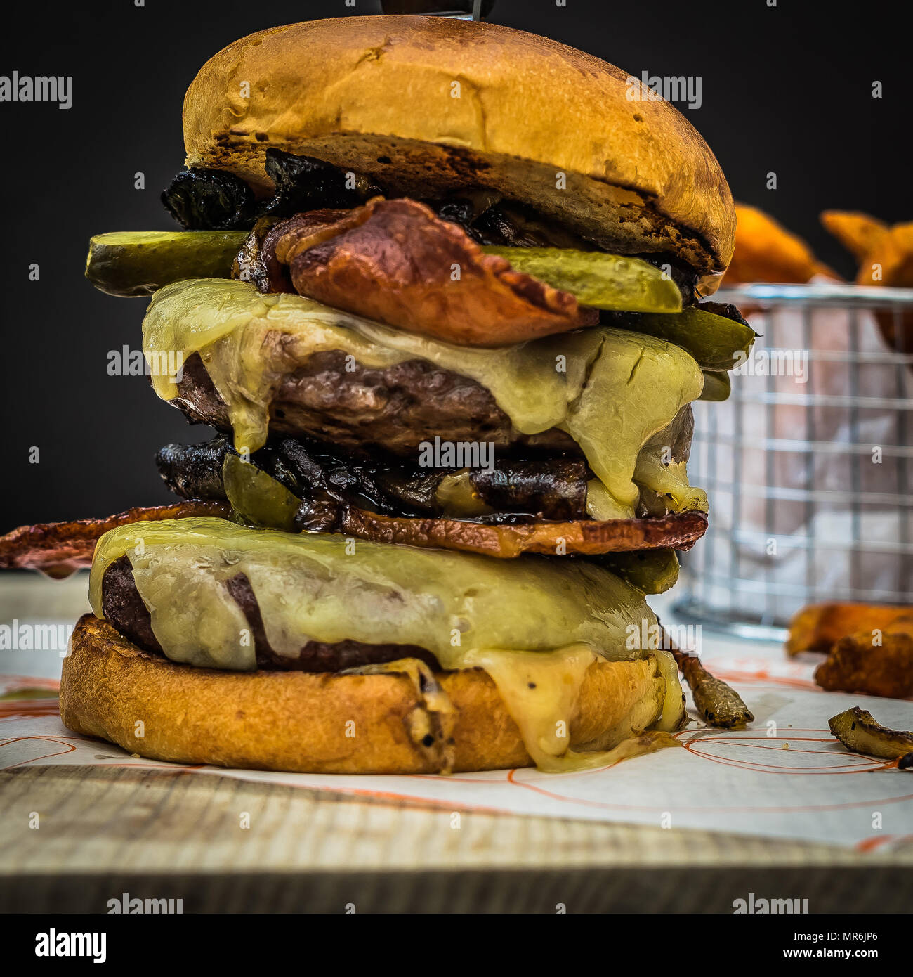 Messy Beef Burger with cheese,bacon,mushrooms and gherkins. Served with a side of sweet potatoes Stock Photo