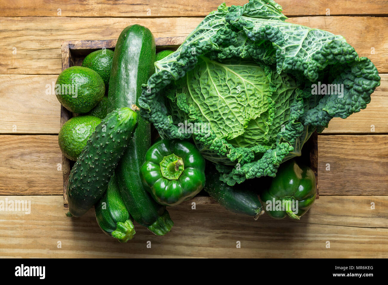Box with Fresh Organic Green Vegetables Savoy Cabbage Zucchini Cucumbers Bell Peppers Avocados on Aged Plank Wood Background. Superfoods Vegan Plant B Stock Photo