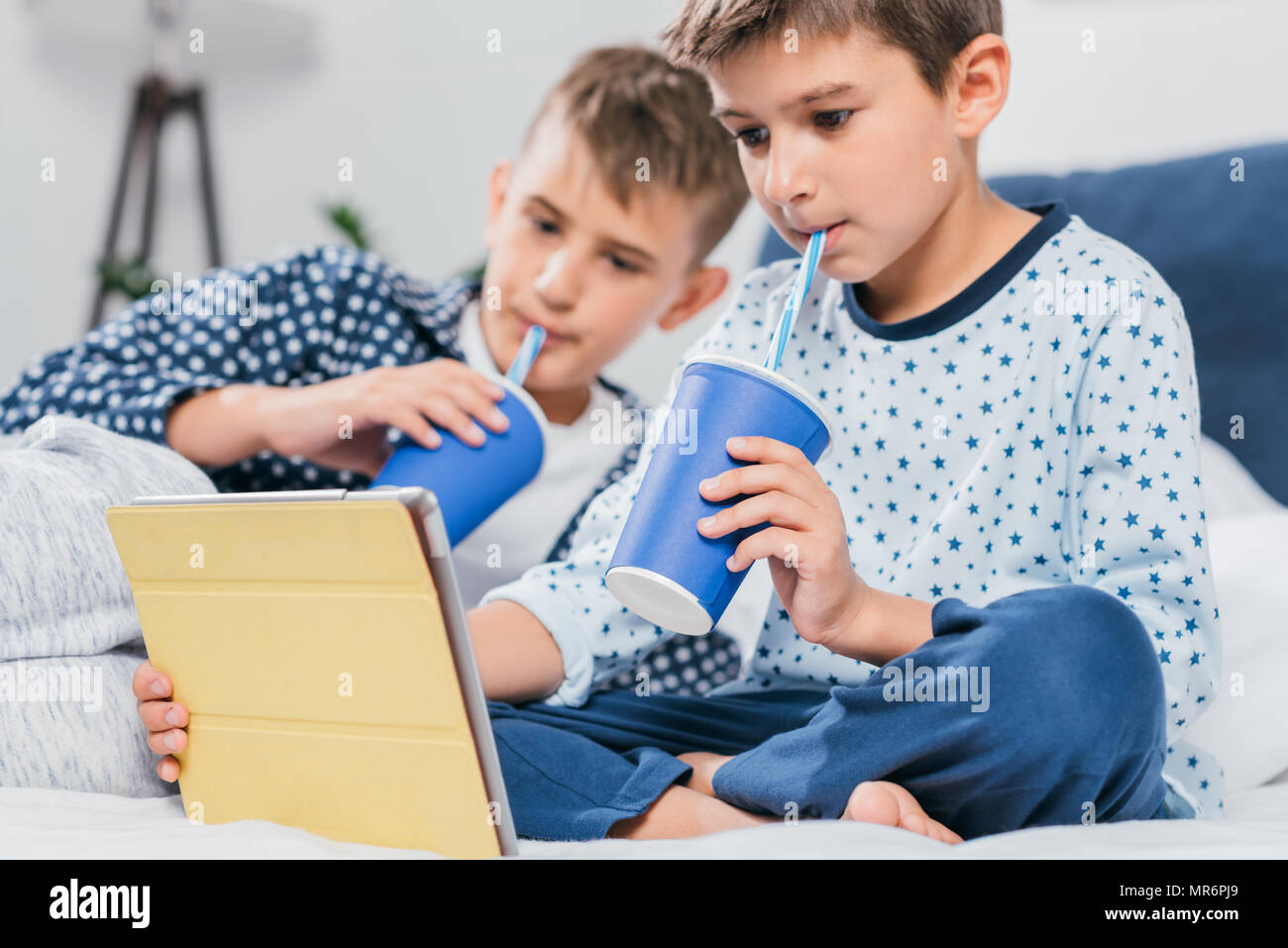 little boys using tablet and drinking soda while lying in bed at home