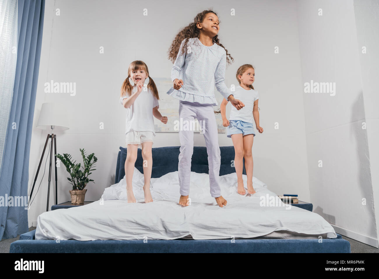 multiethnic little girls in pajamas jumping on bed at home Stock Photo ...