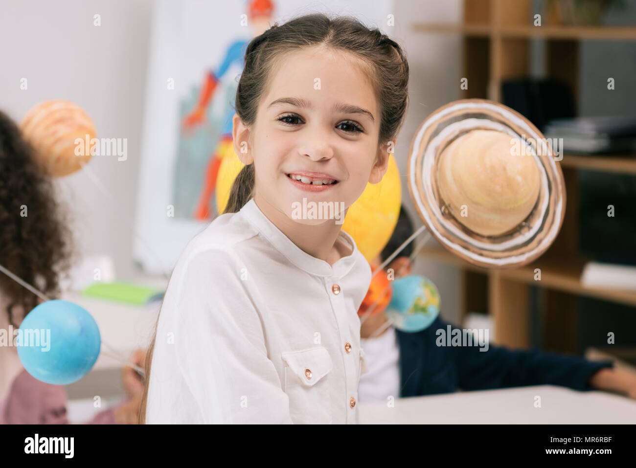 Adorable little schoolgirl smiling at camera while sitting in classroom ...