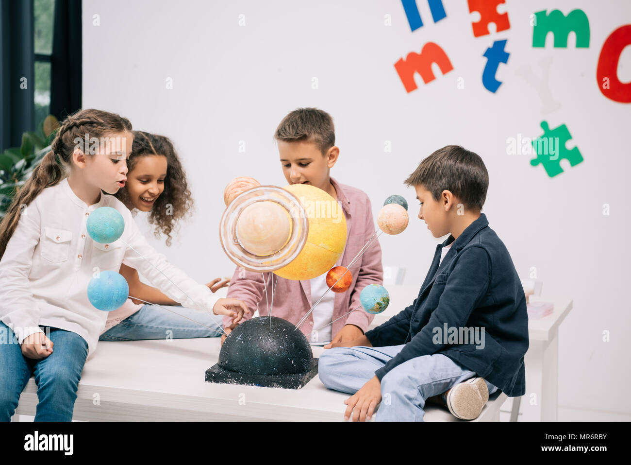 Multiethnic group of schoolchildren working with solar system model in classroom Stock Photo