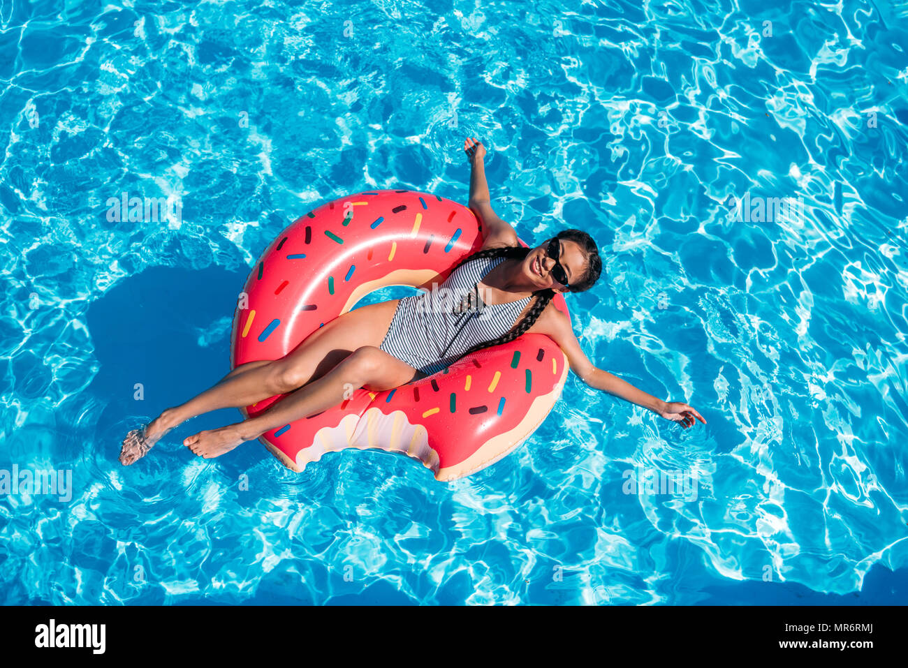 Young asian woman floating on inflatable donut in swimming pool Stock 