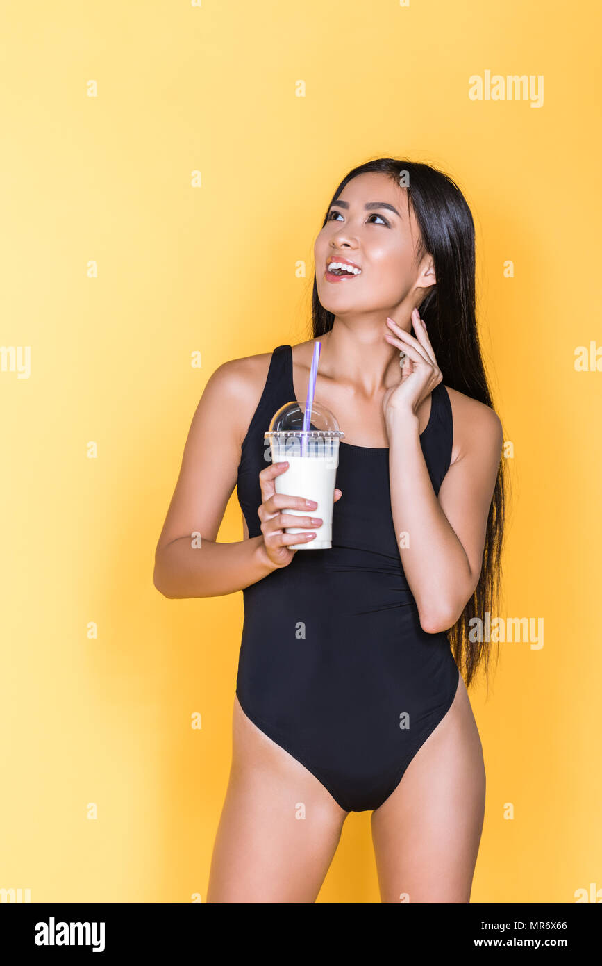 Half-length of smiling asian woman in black swimsuit holding glass of  milkshake and looking up Stock Photo - Alamy