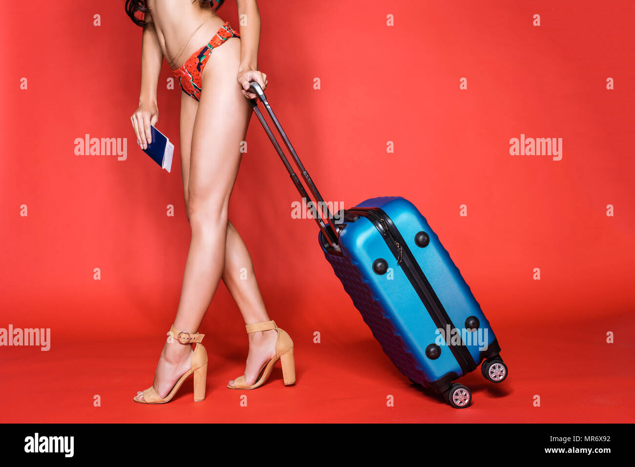 Cropped shot of woman in bright swimsuit and heels, holding a suitcase and airplane tickets Stock Photo