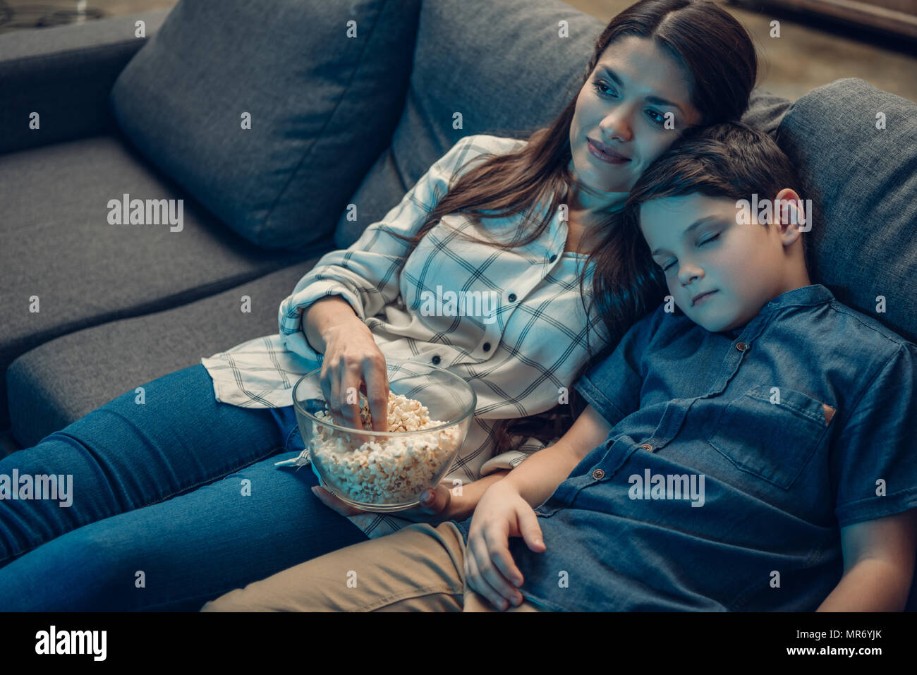 Little boy falling asleep on his mother shoulder while watching tv on