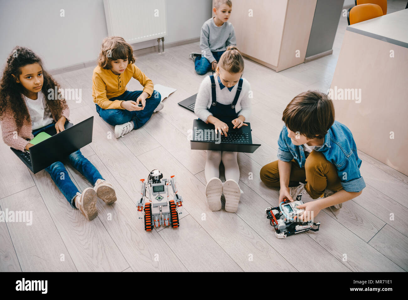 high angle view of kids programming robot while sitting on floor at ...
