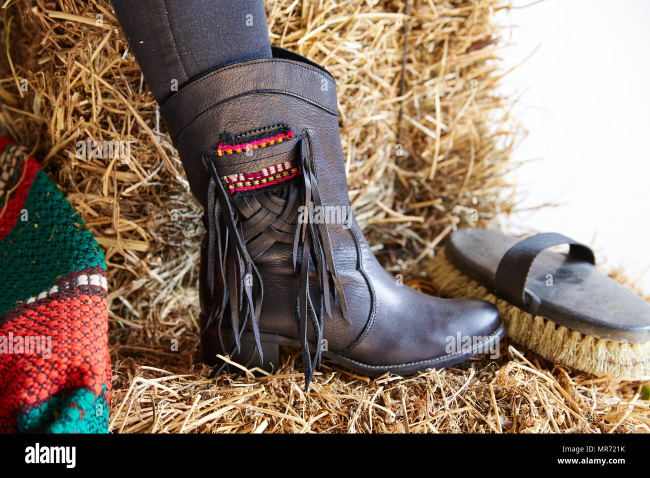 female black boot on stable straw bale with horse brush Stock Photo