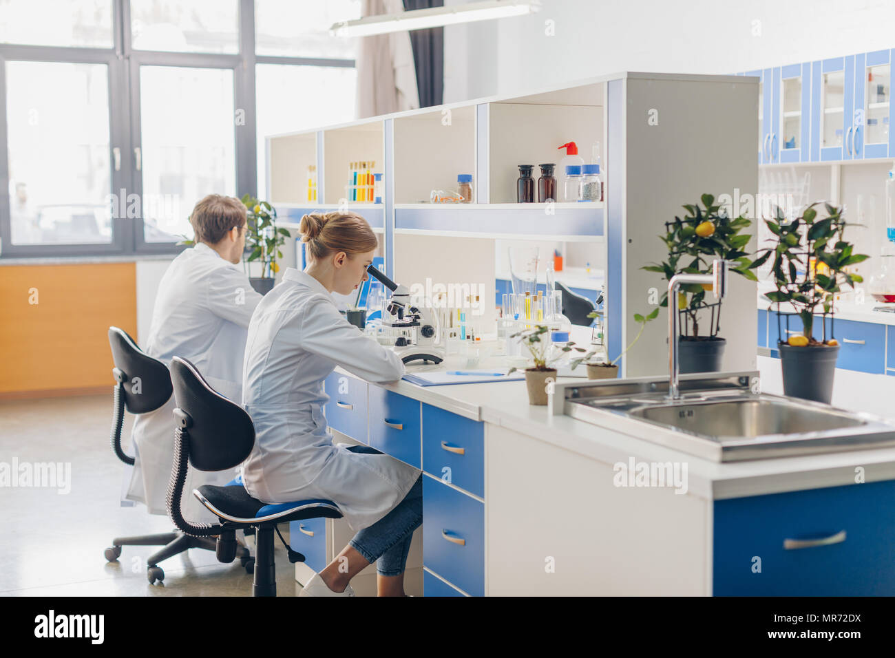 scientists in white coats working with microscope in biological ...