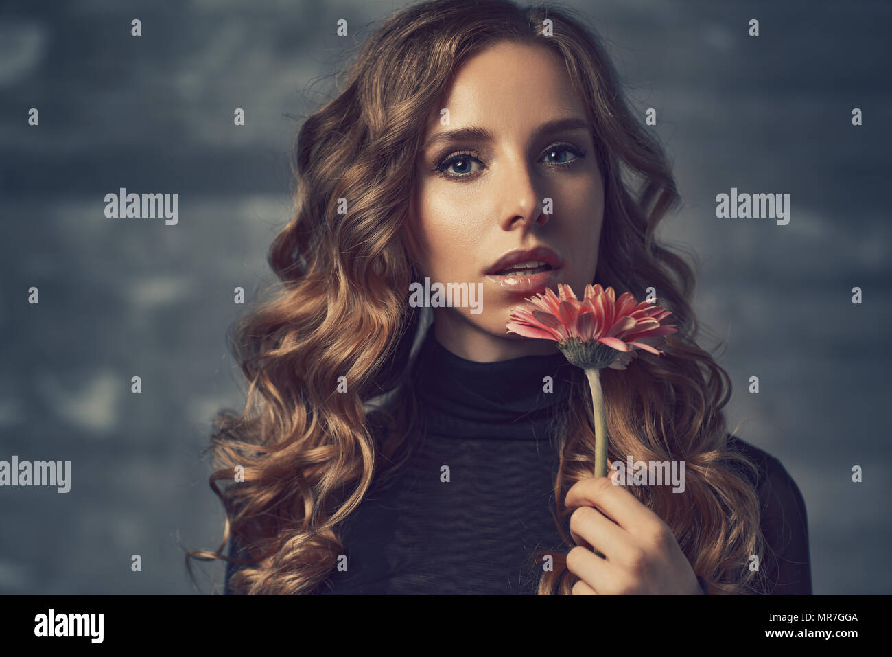 Young woman with flower and curly hair portrait in soft colors Stock Photo