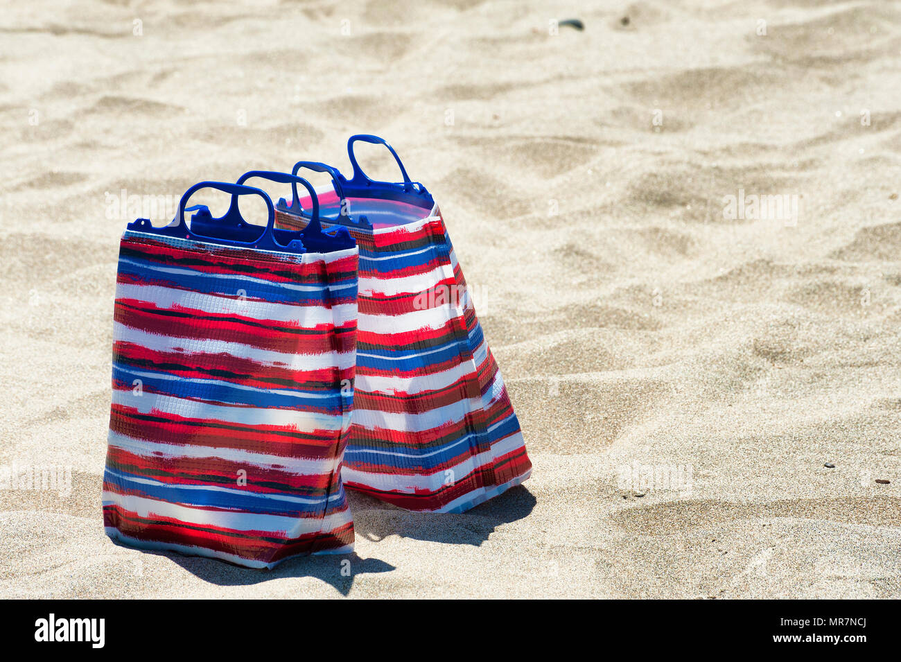 Closeup of two red,white and blue bags sitting on a sandy beach Stock Photo