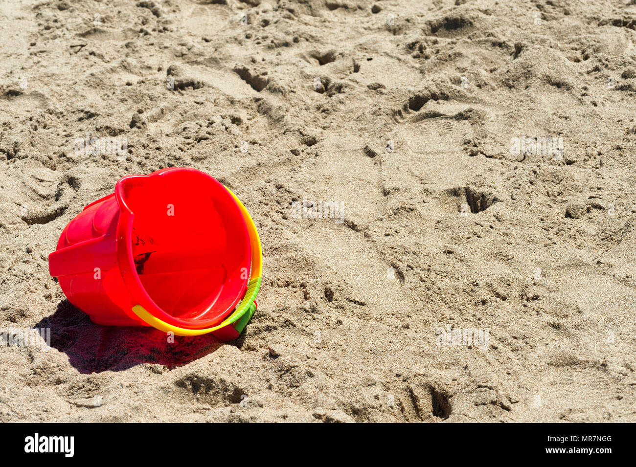 A closeup of a red bucket left on the sandy beach Stock Photo